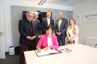 Foto zeigt die Regionalbischöfin Elisabeth Hann von Weyhern beim Eintrag ins Ehrenbuch der Lebenshilfe Nürnberger Land. Hinten, stehend, v. l. Von der Lebenshilfe Nürnberger Land: 1. Vorsitzender Gerhard John, Geschäftsführer Dennis Kummarnitzky, Vorsitzender des Stiftungsvorstands Norbert Dünkel und Dekan Tobias Schäfer, Evang.-Luth. Dekanat Hersbruck und Pfarrerin Gabriele Geyer, Jakobuskriche Schönberg.